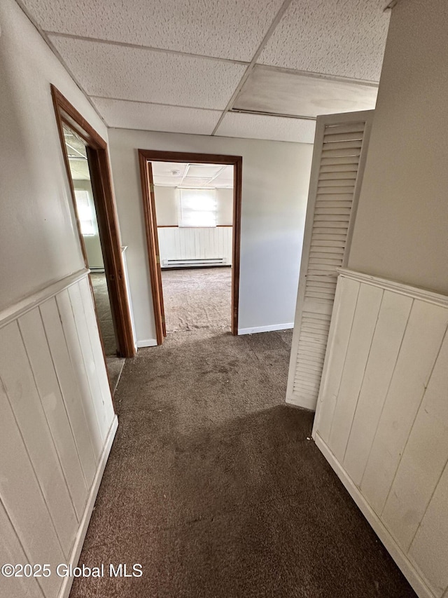 hallway with a drop ceiling, a baseboard heating unit, a wainscoted wall, and carpet floors