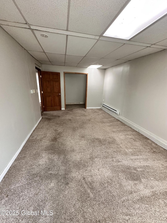 finished below grade area featuring a paneled ceiling, baseboards, carpet floors, and a baseboard radiator