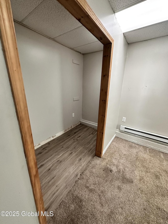 finished basement featuring baseboard heating, carpet flooring, a paneled ceiling, and baseboards