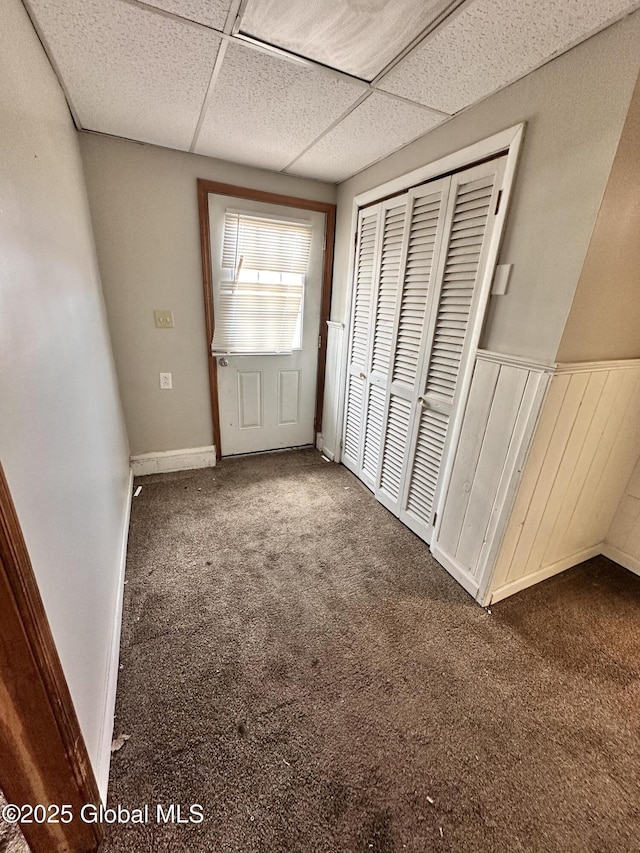 unfurnished bedroom with carpet flooring, a closet, a drop ceiling, and wainscoting