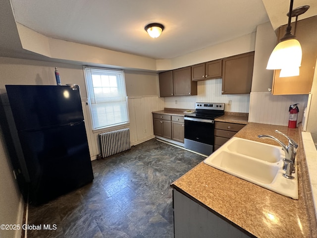 kitchen featuring a wainscoted wall, radiator heating unit, freestanding refrigerator, a sink, and stainless steel range with electric cooktop