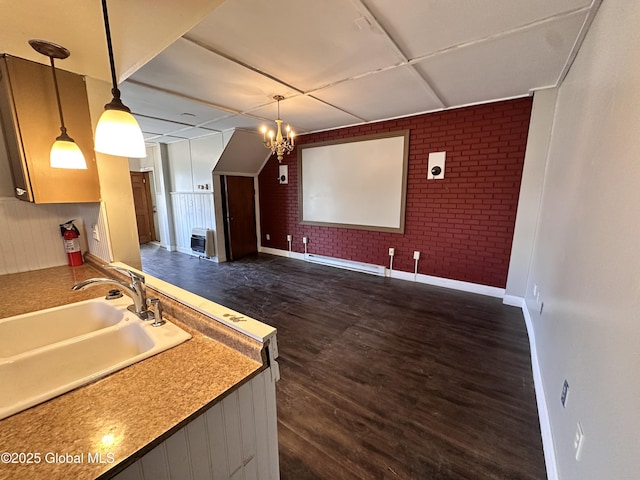 kitchen featuring a sink, dark wood-style floors, an inviting chandelier, brick wall, and hanging light fixtures