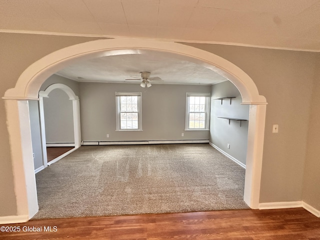 unfurnished room featuring wood finished floors, carpet floors, arched walkways, ceiling fan, and baseboard heating