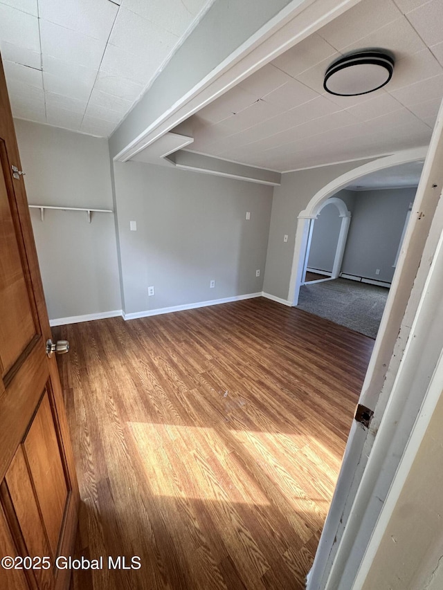 empty room with wood finished floors, arched walkways, and baseboards