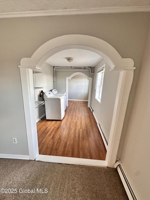 hallway with arched walkways, baseboard heating, washing machine and dryer, and wood finished floors