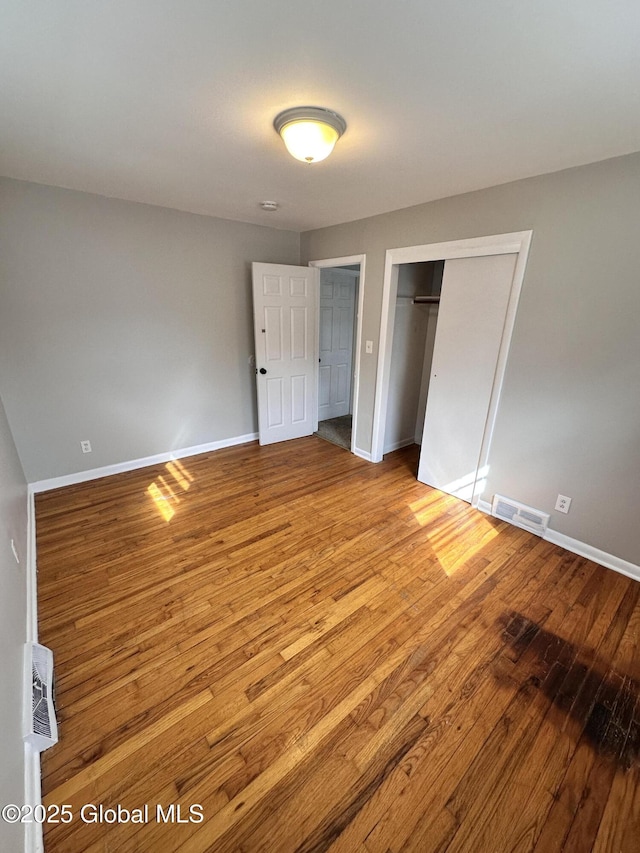 unfurnished bedroom featuring a closet, visible vents, baseboards, and wood finished floors