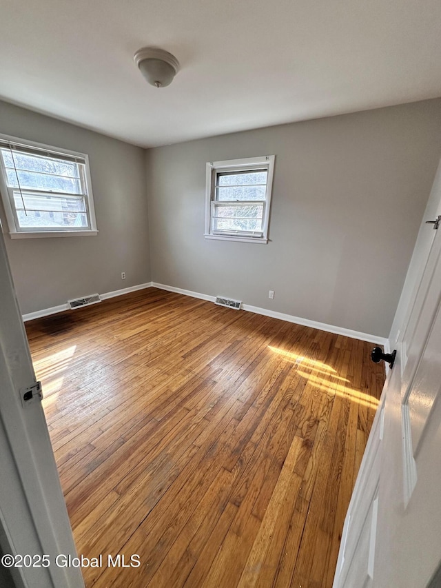 unfurnished room with visible vents, baseboards, and hardwood / wood-style floors