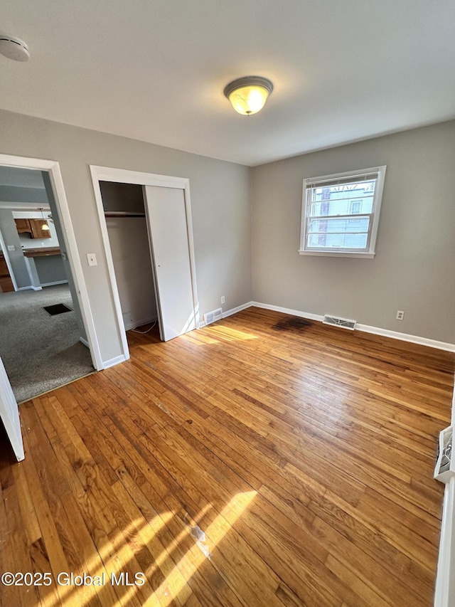 unfurnished bedroom featuring wood finished floors, visible vents, a closet, and baseboards