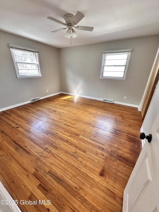 unfurnished room with hardwood / wood-style flooring, baseboards, visible vents, and ceiling fan