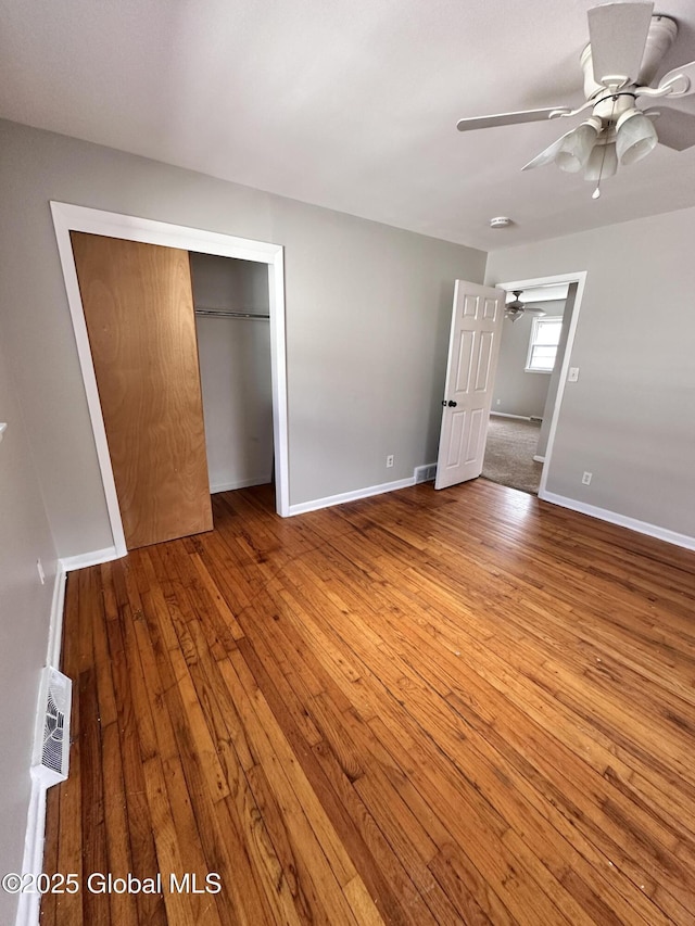 unfurnished bedroom featuring a ceiling fan, baseboards, a closet, and wood-type flooring