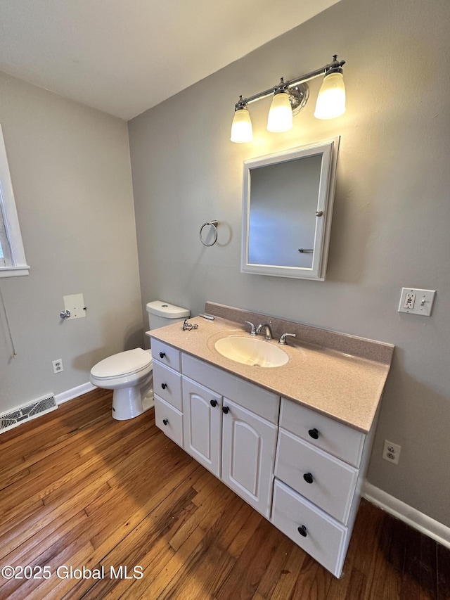 half bath with visible vents, toilet, wood finished floors, baseboards, and vanity