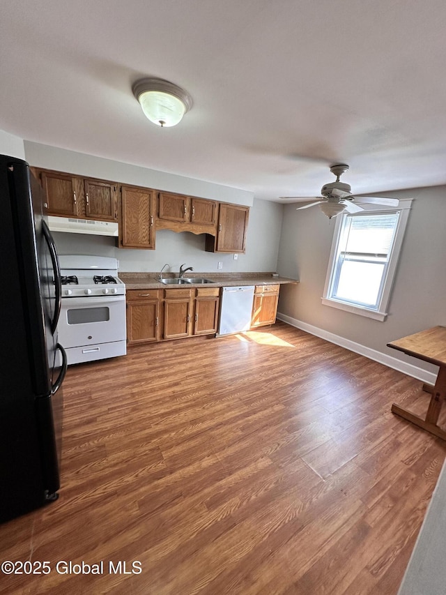 kitchen featuring a sink, under cabinet range hood, white gas range oven, freestanding refrigerator, and dishwashing machine