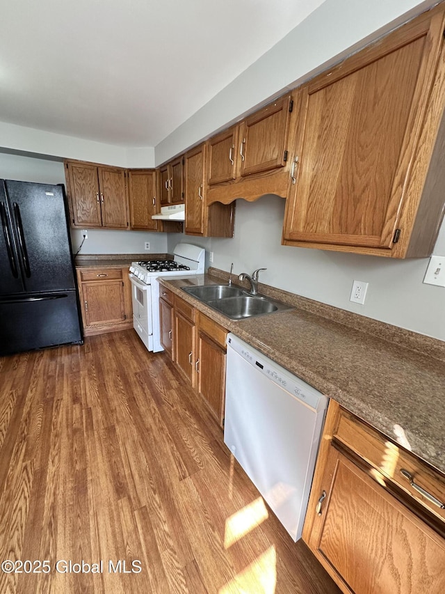 kitchen featuring white appliances, dark wood finished floors, a sink, under cabinet range hood, and brown cabinets