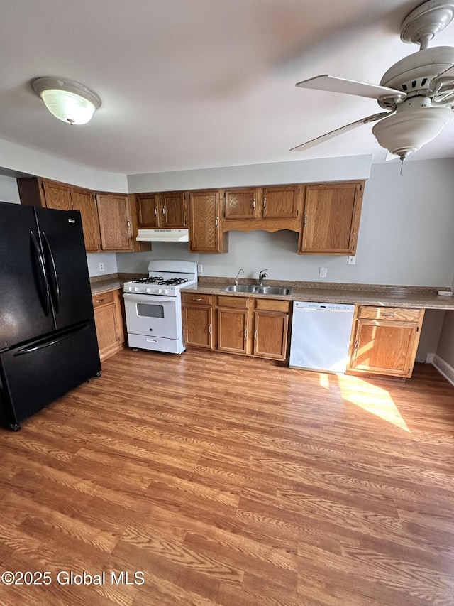 kitchen featuring white appliances, wood finished floors, a sink, under cabinet range hood, and brown cabinets