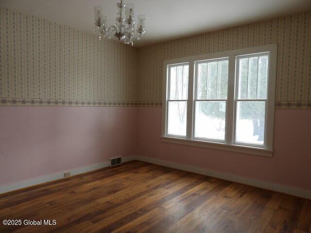 unfurnished room featuring visible vents, a notable chandelier, wood finished floors, and wallpapered walls