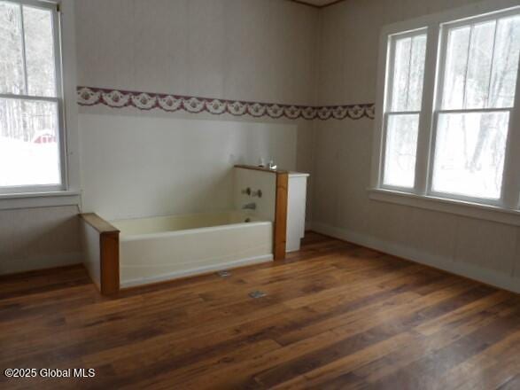 bathroom with a bath, wood finished floors, baseboards, and a healthy amount of sunlight