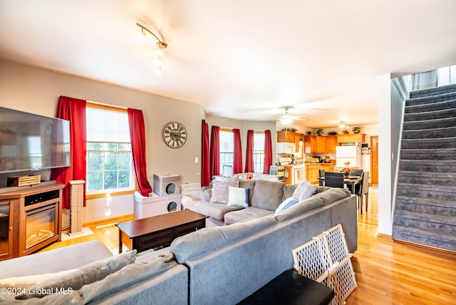 living room with a wealth of natural light, a ceiling fan, stairs, and light wood finished floors