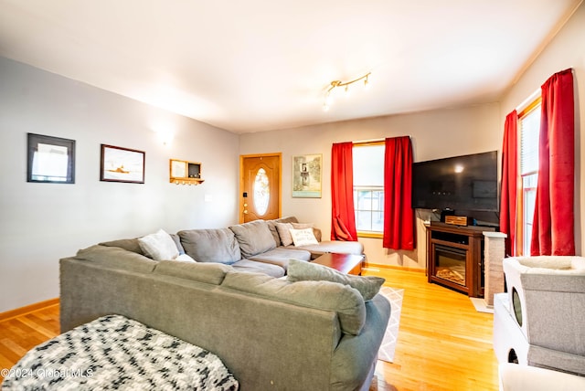 living area with a glass covered fireplace, baseboards, and light wood-type flooring