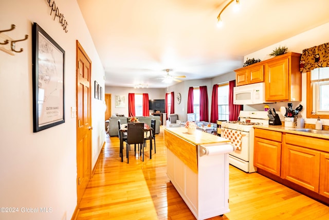 kitchen featuring a kitchen island, light countertops, light wood-type flooring, white appliances, and a ceiling fan