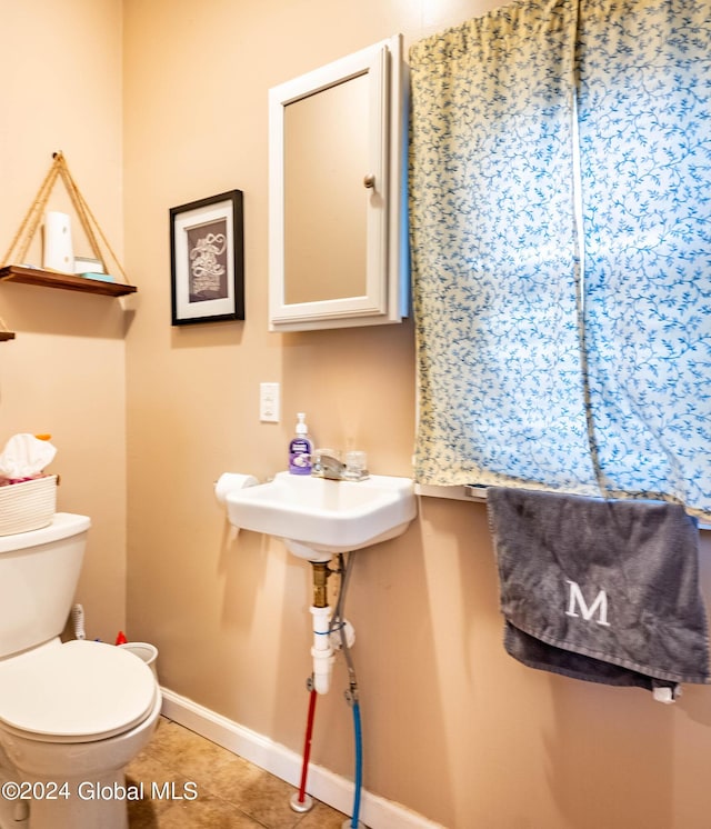 half bathroom featuring tile patterned flooring, toilet, baseboards, and a sink