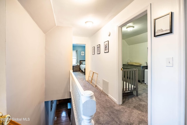 hallway featuring an upstairs landing, visible vents, carpet flooring, and vaulted ceiling