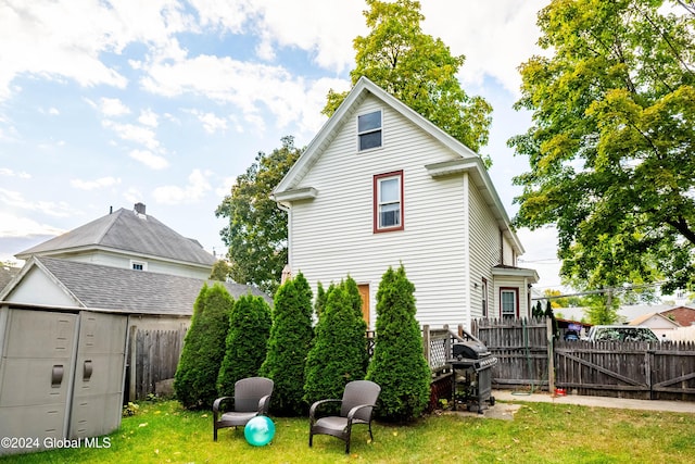 rear view of house featuring an outbuilding, fence, a lawn, and a shed