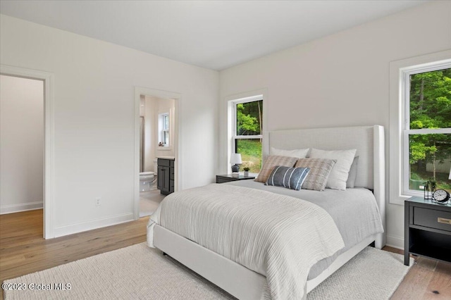 bedroom featuring multiple windows, wood finished floors, baseboards, and connected bathroom