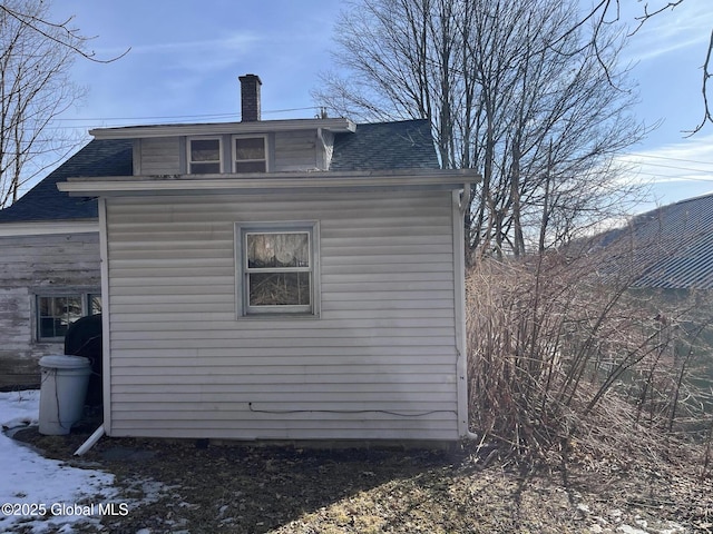 view of side of home featuring a chimney and a shingled roof