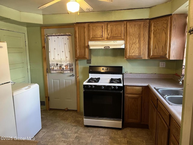 kitchen featuring under cabinet range hood, brown cabinets, gas stove, fridge, and a sink