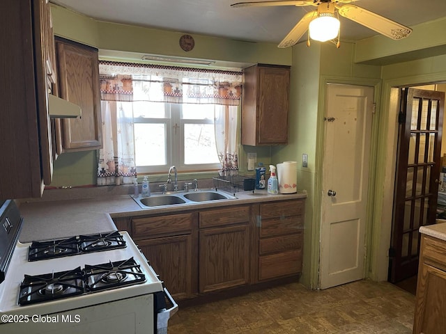 kitchen featuring a ceiling fan, gas range gas stove, a sink, extractor fan, and brown cabinets