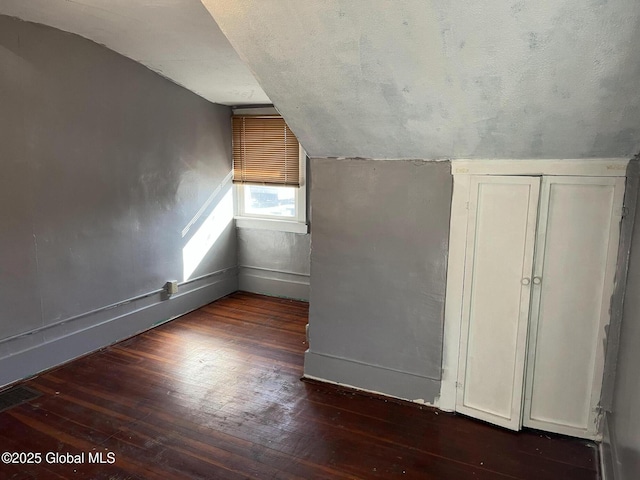 additional living space featuring visible vents, lofted ceiling, hardwood / wood-style flooring, a textured ceiling, and baseboards