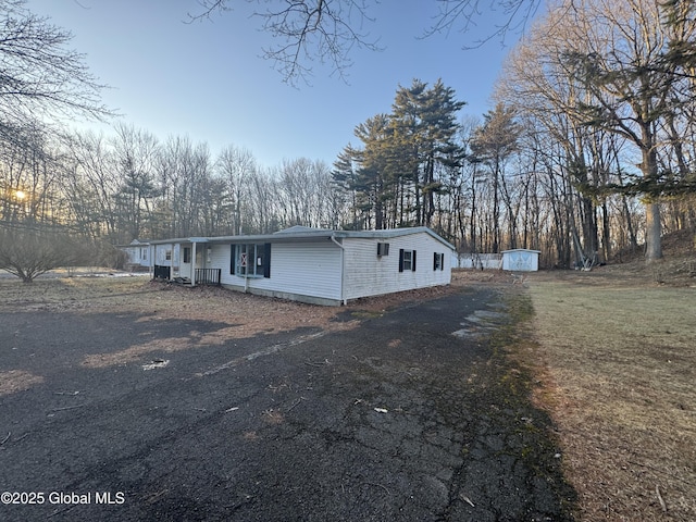 view of front of house featuring aphalt driveway, an outdoor structure, a front lawn, and a shed