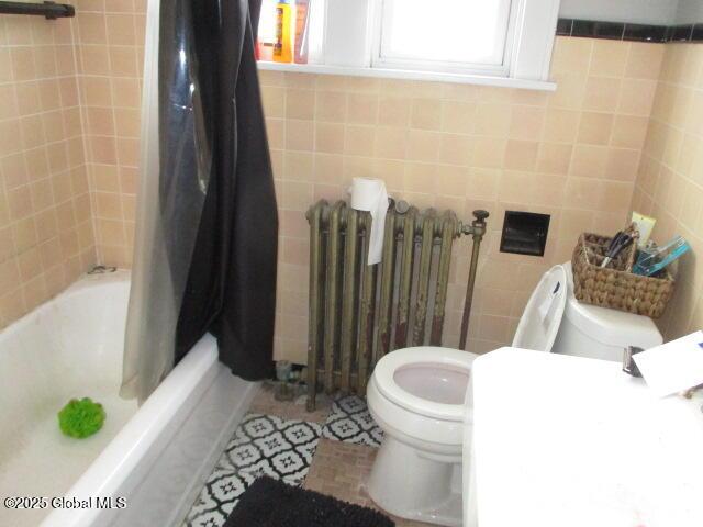 bathroom with tile patterned floors, shower / bath combo with shower curtain, toilet, radiator, and tile walls