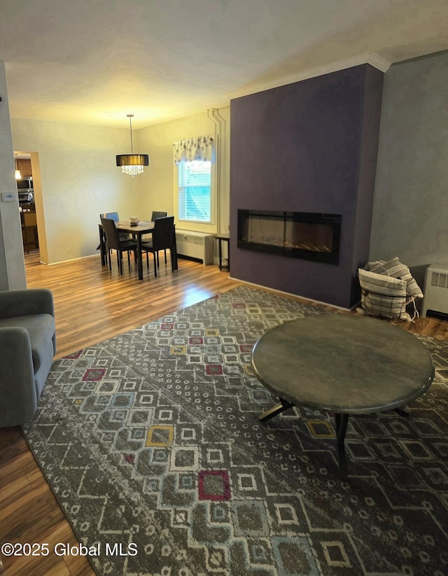 living room featuring a glass covered fireplace, radiator, an inviting chandelier, and wood finished floors