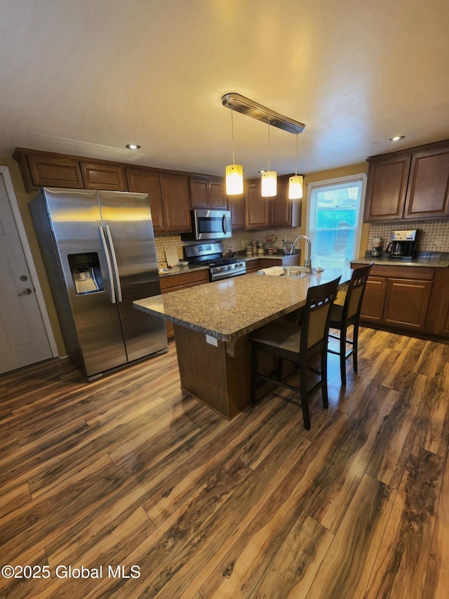 kitchen featuring light stone counters, decorative backsplash, dark wood-style flooring, appliances with stainless steel finishes, and a sink