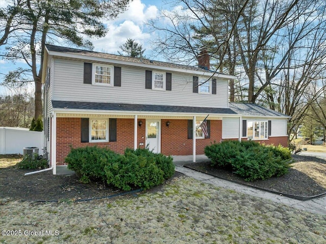 view of front of house with brick siding, fence, central air condition unit, covered porch, and a chimney