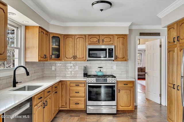 kitchen with ornamental molding, a sink, light countertops, glass insert cabinets, and appliances with stainless steel finishes