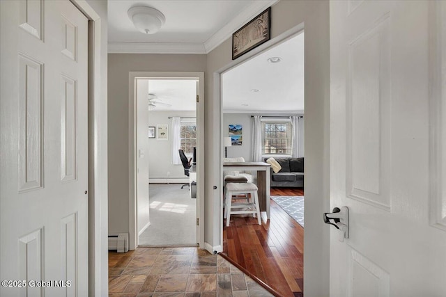 hallway featuring crown molding, stone finish floor, baseboards, and baseboard heating