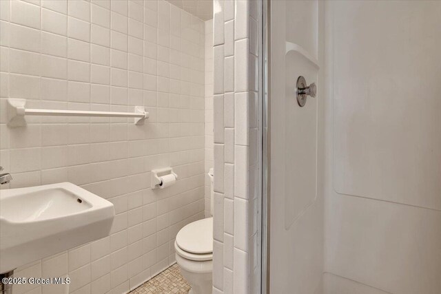 full bath featuring tile patterned floors, toilet, tile walls, and a shower stall