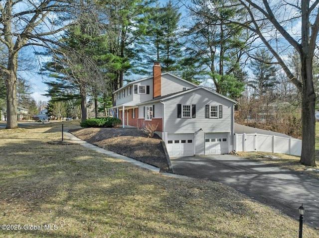 view of side of home with aphalt driveway, a chimney, an attached garage, and fence