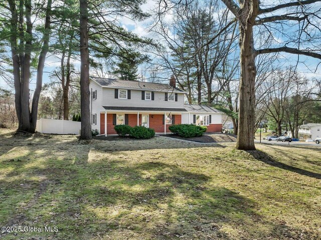 traditional-style home featuring a front yard, brick siding, a chimney, and fence