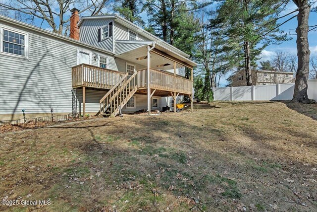 rear view of house featuring a chimney, stairway, a wooden deck, and fence