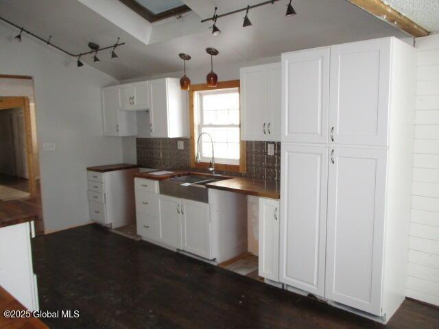 kitchen featuring pendant lighting, a sink, backsplash, white cabinets, and rail lighting