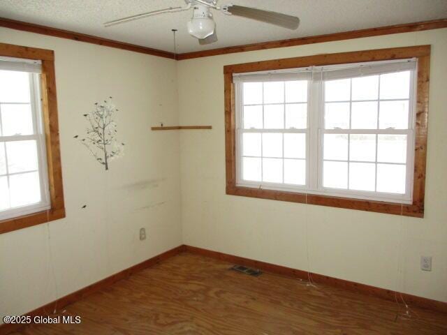 unfurnished room with a wealth of natural light, visible vents, and wood finished floors