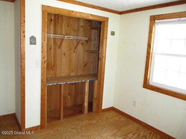 unfurnished bedroom featuring a closet, multiple windows, crown molding, and baseboards