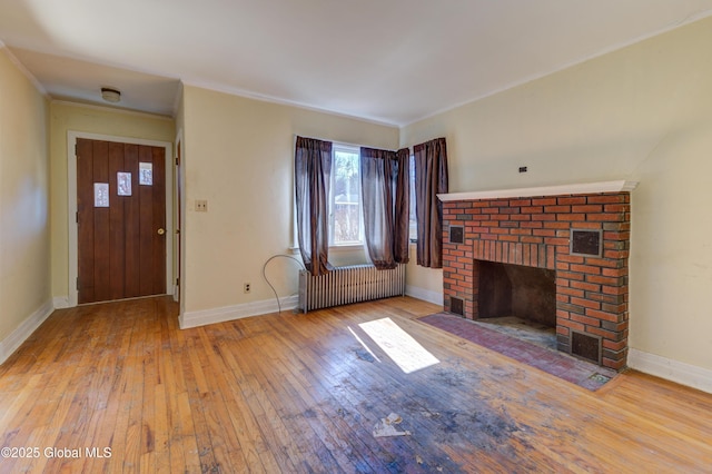 unfurnished living room featuring a brick fireplace, crown molding, baseboards, radiator heating unit, and hardwood / wood-style floors