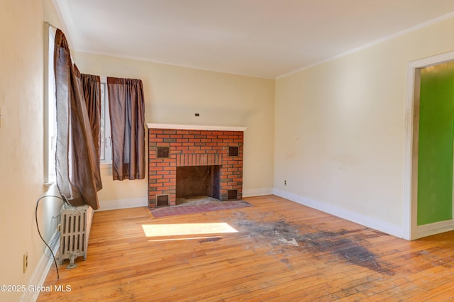 unfurnished living room featuring radiator, hardwood / wood-style flooring, baseboards, and a brick fireplace