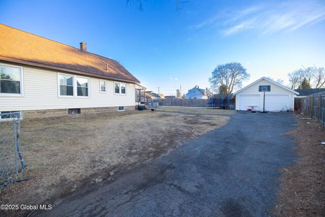 view of side of home with a detached garage, a trampoline, a fenced backyard, an outdoor structure, and a chimney