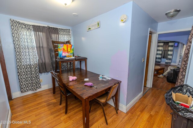 dining space featuring arched walkways, light wood-style flooring, and baseboards