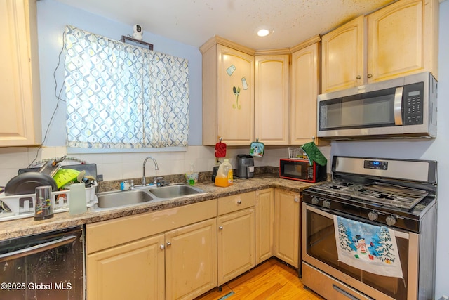 kitchen featuring light brown cabinetry, a sink, backsplash, stainless steel appliances, and light wood-style floors